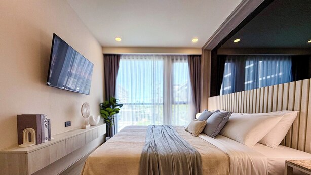 Une chambre d’hôtel moderne dotée d’un grand lit, d’un téléviseur à écran plat fixé au mur, d’une table de chevet et d’une fenêtre avec des rideaux.