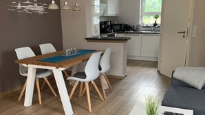Ein modernes Wohnzimmer mit Essbereich und einer Küche im Hintergrund, dazu ein graues Sofa.