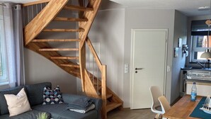 Ein modernes Wohnzimmer mit einer Holztreppe, einem grauen Sofa, einem Esstisch und einer Küchenzeile.