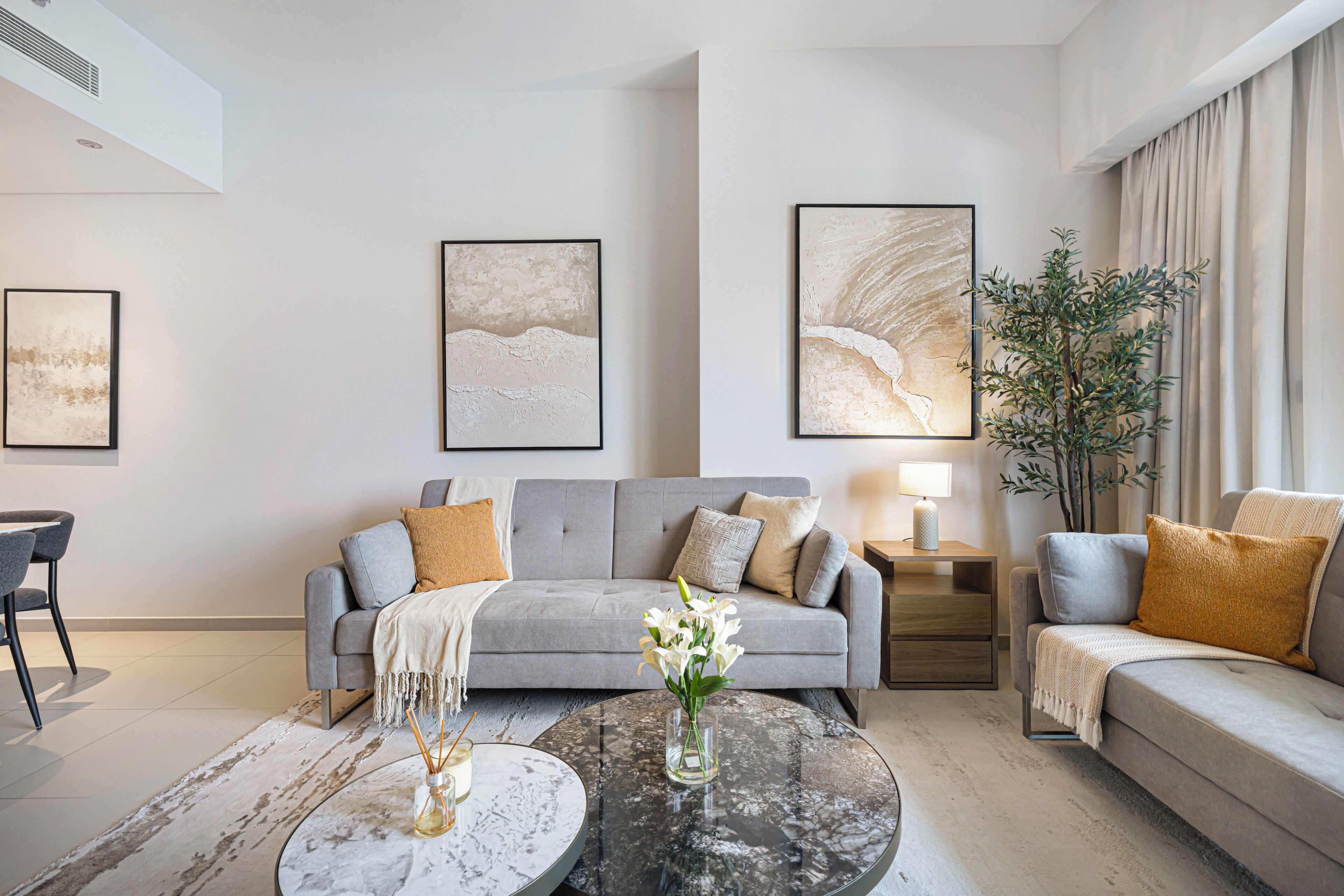 Ein modernes Wohnzimmer mit einem grauen Sofa, einem runden Couchtisch und zwei gerahmten abstrakten Gemälden an der Wand.