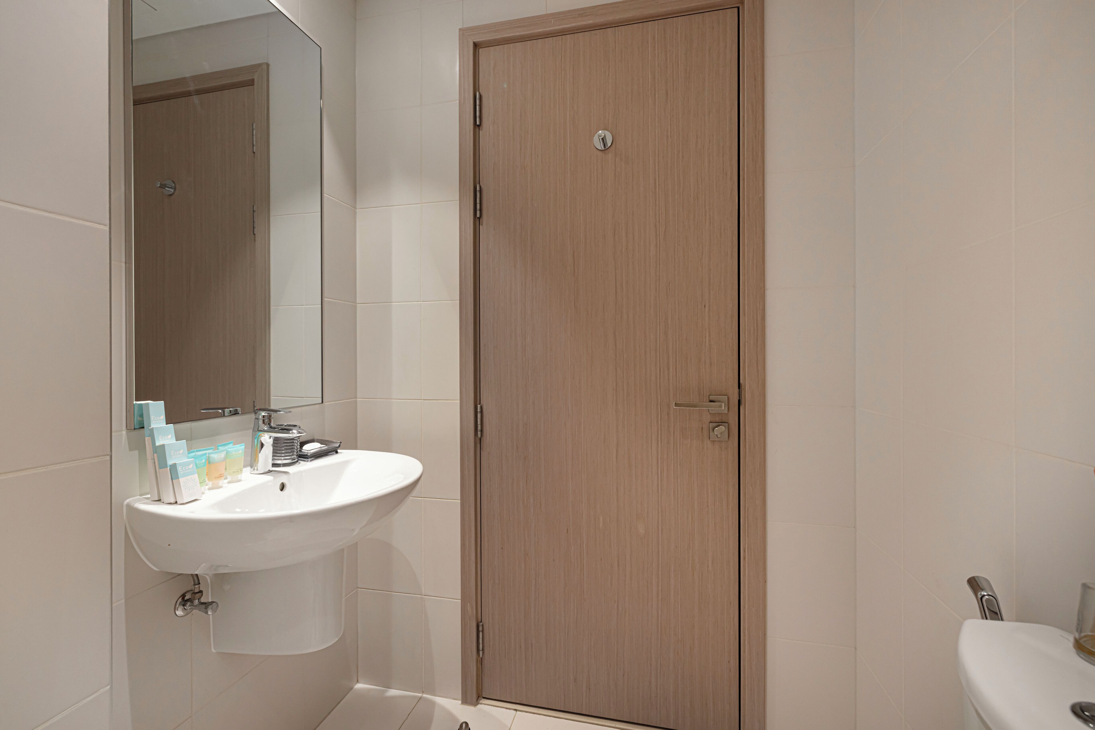 Un baño con puerta de madera, un lavabo blanco y un espejo.