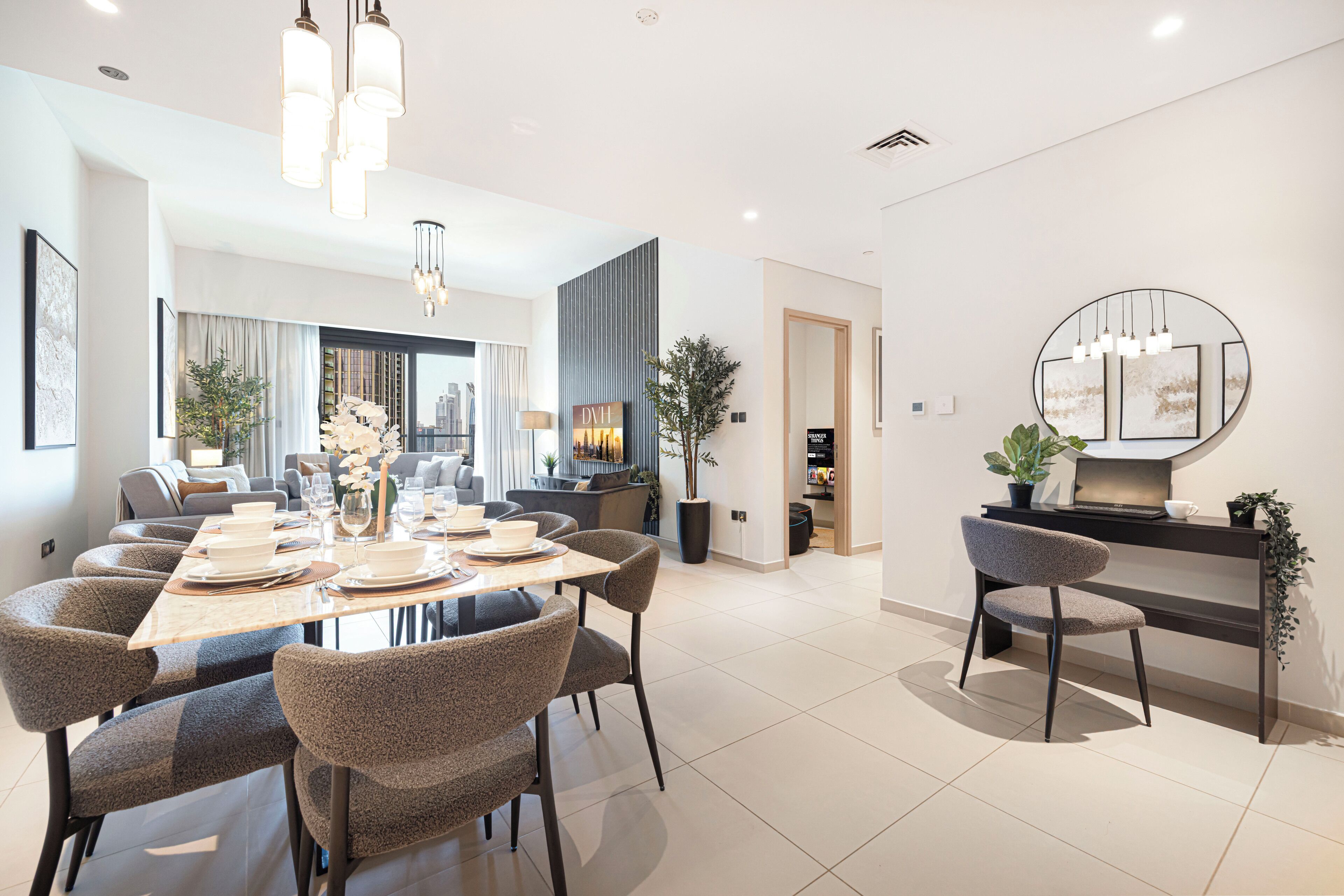 A modern dining area with a long table set for six, surrounded by upholstered chairs, with a cityscape view through large windows.