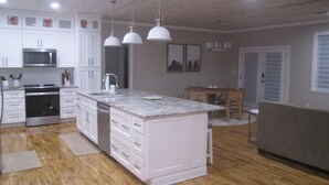 A modern kitchen with white cabinetry, a central island, stainless steel appliances, pendant lighting, and a dining area with a wooden table and chairs.