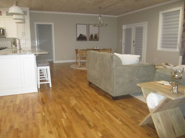 A spacious living area with a grey sofa, wooden dining table, and a kitchen area with white cabinets and a built-in island. - Clean & Cute New Home! 3-bed in Blue Ridge.7min to downtown BR, 20min to Ellijay (Blue Ridge)