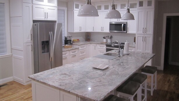 A modern kitchen with white cabinets, stainless steel appliances, a marble countertop, and pendant lighting.