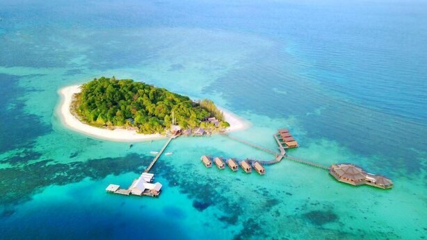 An aerial view of a tropical island with a white sandy beach, lush green vegetation, and a dock leading to a series of overwater bungalows. - Lankayan Island Dive Resort (Sandakan)
