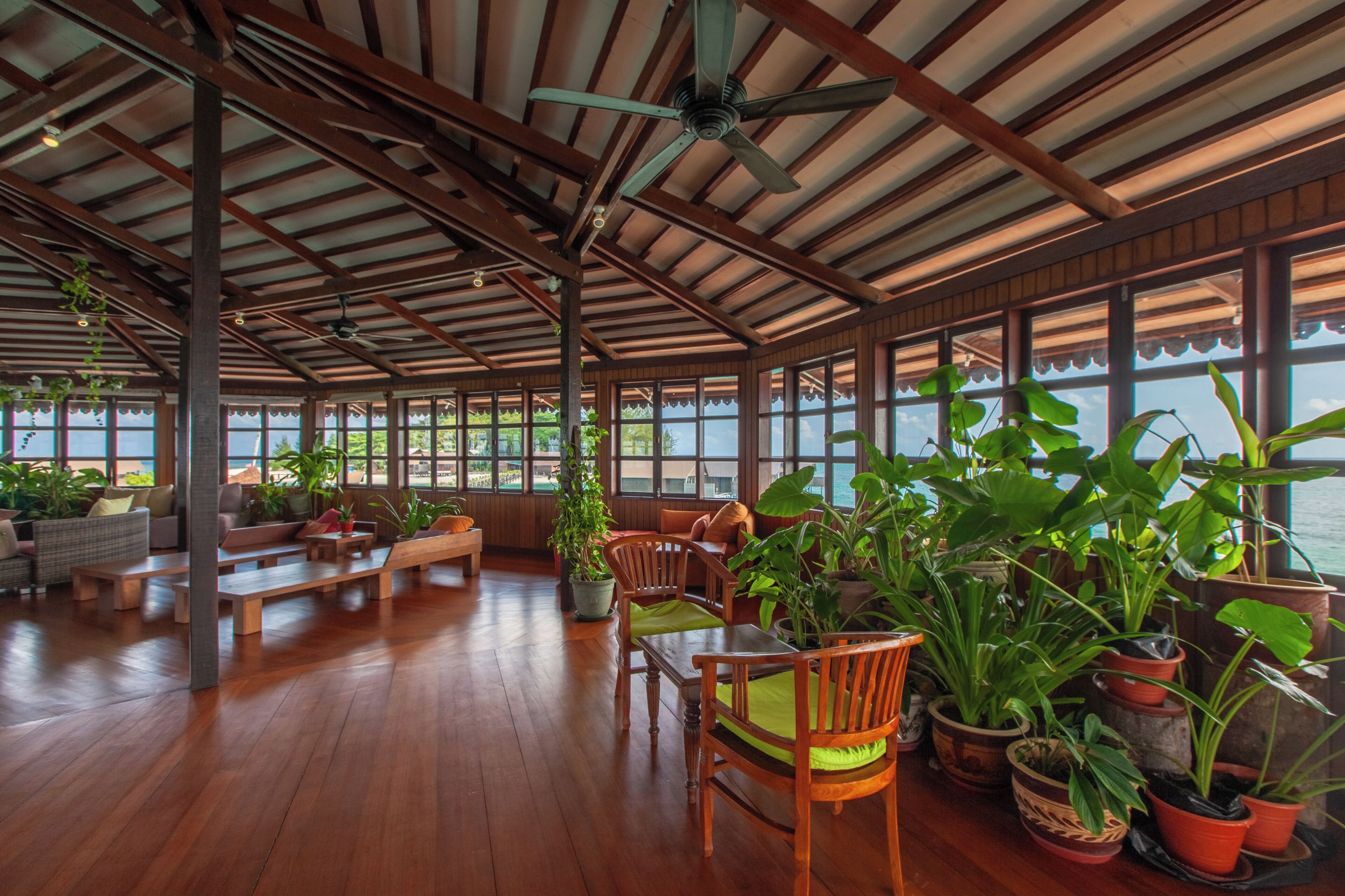 A spacious indoor area with wooden flooring, multiple seating arrangements, and potted plants.