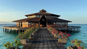 A wooden overwater structure with a central entrance, flanked by potted plants and leading to a pier extending into the sea. - Lankayan Island Dive Resort (Sandakan)