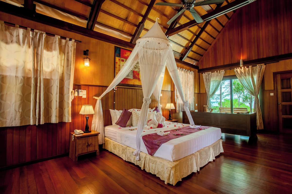 Ein geräumiges Schlafzimmer mit Baldachinbett, Holzboden und einem großen Fenster mit Vorhängen.