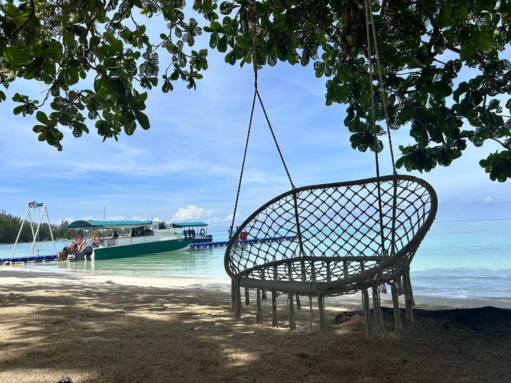 A beach with a swing chair, a boat, and a clear view of the ocean.