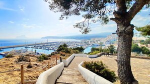 A coastal town with a marina, a staircase leading down to the water, and a view of the sea and distant buildings. - Azurea M A - Benitachell-Poble Nou de Benitatxell (el), Costa Blanca (Benitachell-Poble Nou de Benitatxell (el))