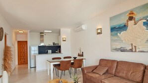 A modern living room with a brown leather sofa, a dining area with a white table and chairs, and a kitchen in the background. - Azurea M A - Benitachell-Poble Nou de Benitatxell (el), Costa Blanca (Benitachell-Poble Nou de Benitatxell (el))