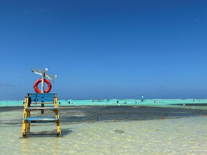 Een bewakershut met een rode reddingsboei en een vin van een haai aan een strand met helder turquoise water.