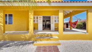 A yellow building with a covered entrance, a hammock, and a staircase leading to the entrance. - Villa Sugar Garden (Kralendijk)
