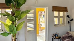 A room with a large potted plant, a colorful painting, a sofa, and a small table with a lamp. - Villa Sugar Garden (Kralendijk)