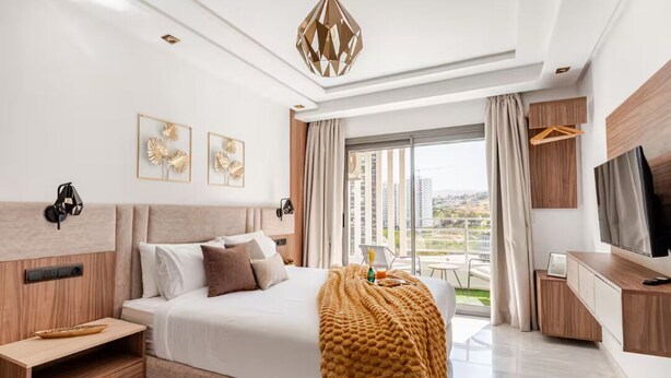 Een moderne hotelkamer met een groot bed, een televisie, een bureau en een balkon met uitzicht op de stad.