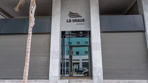 A modern building with a sign reading "LA VAGUE RÉSIDENCE" and a glass entrance reflecting parked cars.
