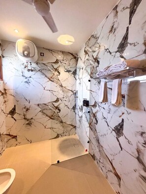 A bathroom with a marble wall, a glass shower enclosure, a toilet, and a towel rack. - THE ELET (Amritsar)
