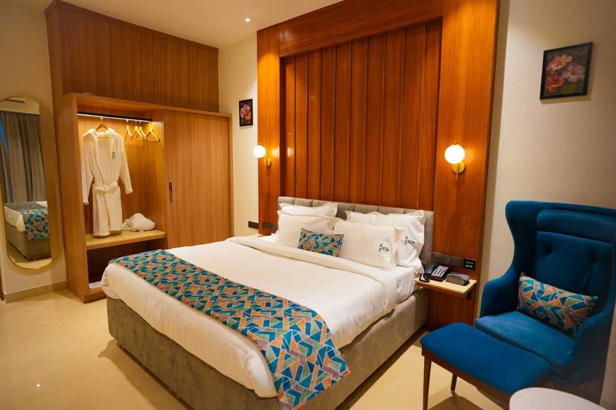 A hotel room with a bed, a blue armchair, a wooden wardrobe, and a mirror.