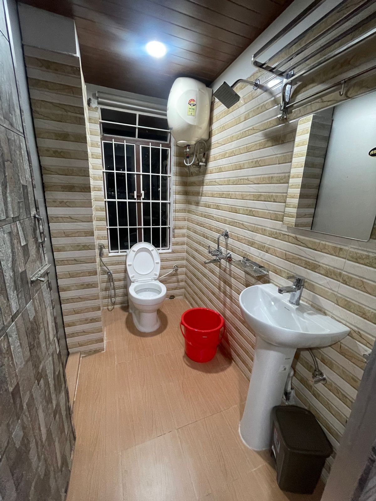 Ein kleines Badezimmer mit Toilette, Waschbecken und einem roten Eimer.