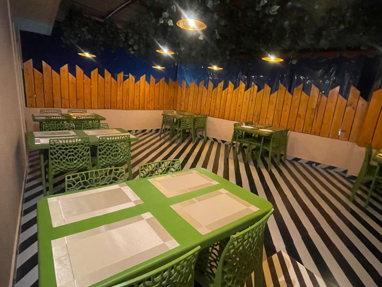 A dining area with green tables and chairs, a striped floor, and a wooden wall with a blue and orange design.
