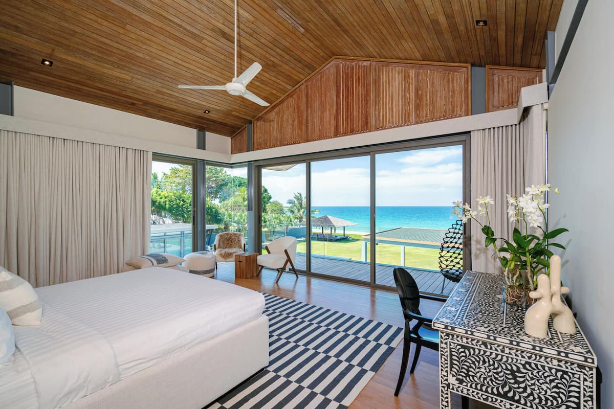 A modern bedroom with a large bed, a desk with a view, and a ceiling fan.