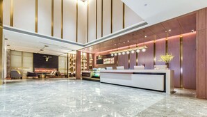 Un hall d’entrée spacieux avec un sol en marbre, un comptoir d’accueil, un espace salon et une cheminée.