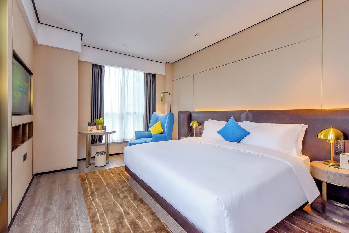 Ein Hotelzimmer mit einem großen Bett, einem Schreibtisch, einem Sessel und einem Fernseher.