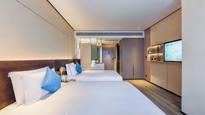 Une chambre d’hôtel moderne avec deux lits, une télévision et une salle de bain visible à travers une porte ouverte.