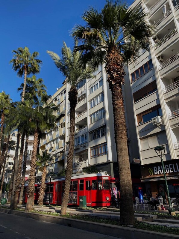 A multi-story building with balconies, palm trees, and a red tram. - Maxihomes Hadrian Olive (Antalya)