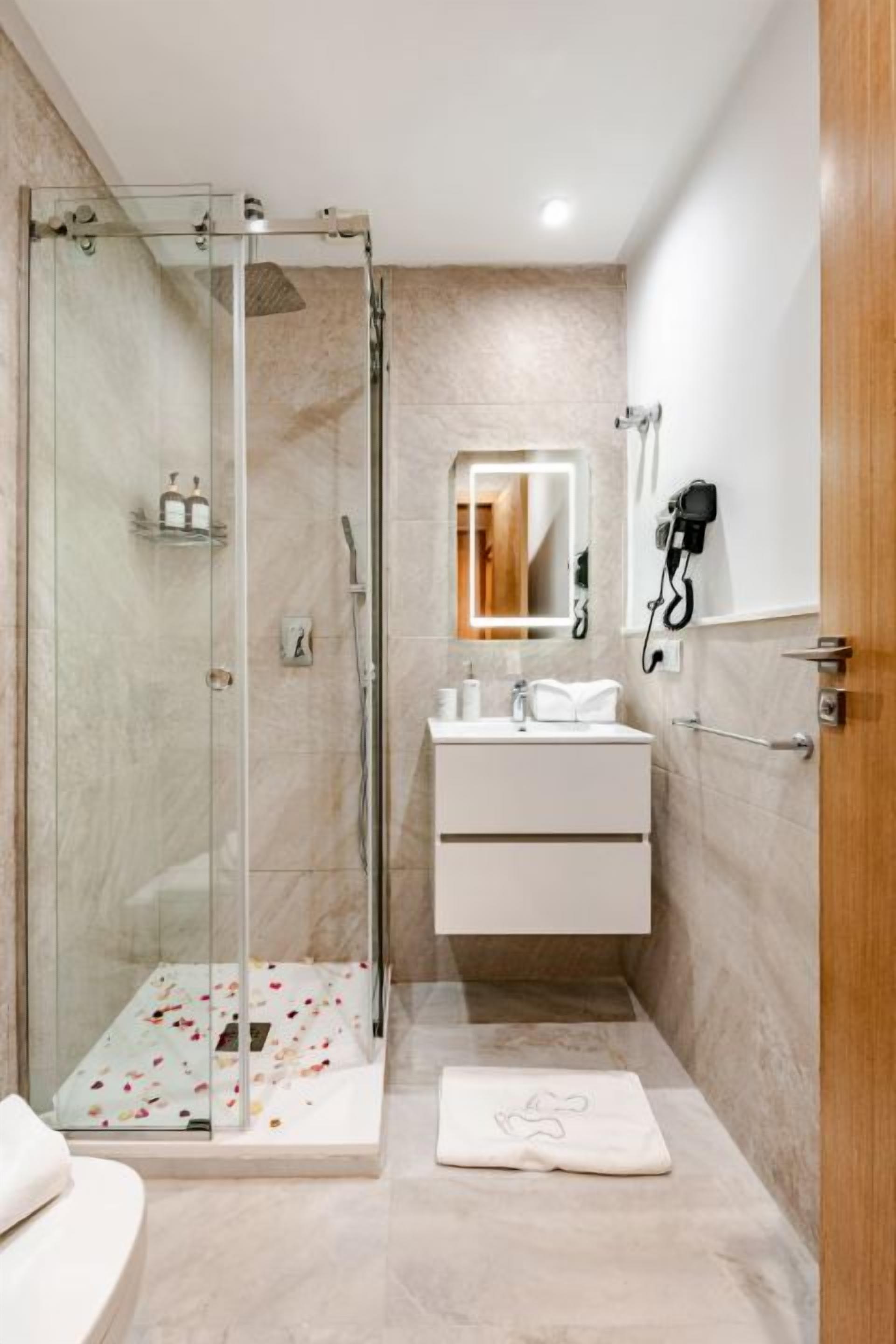 Een moderne badkamer met een glazen douchecabine, een witte wastafel met spiegel en een houten deur.