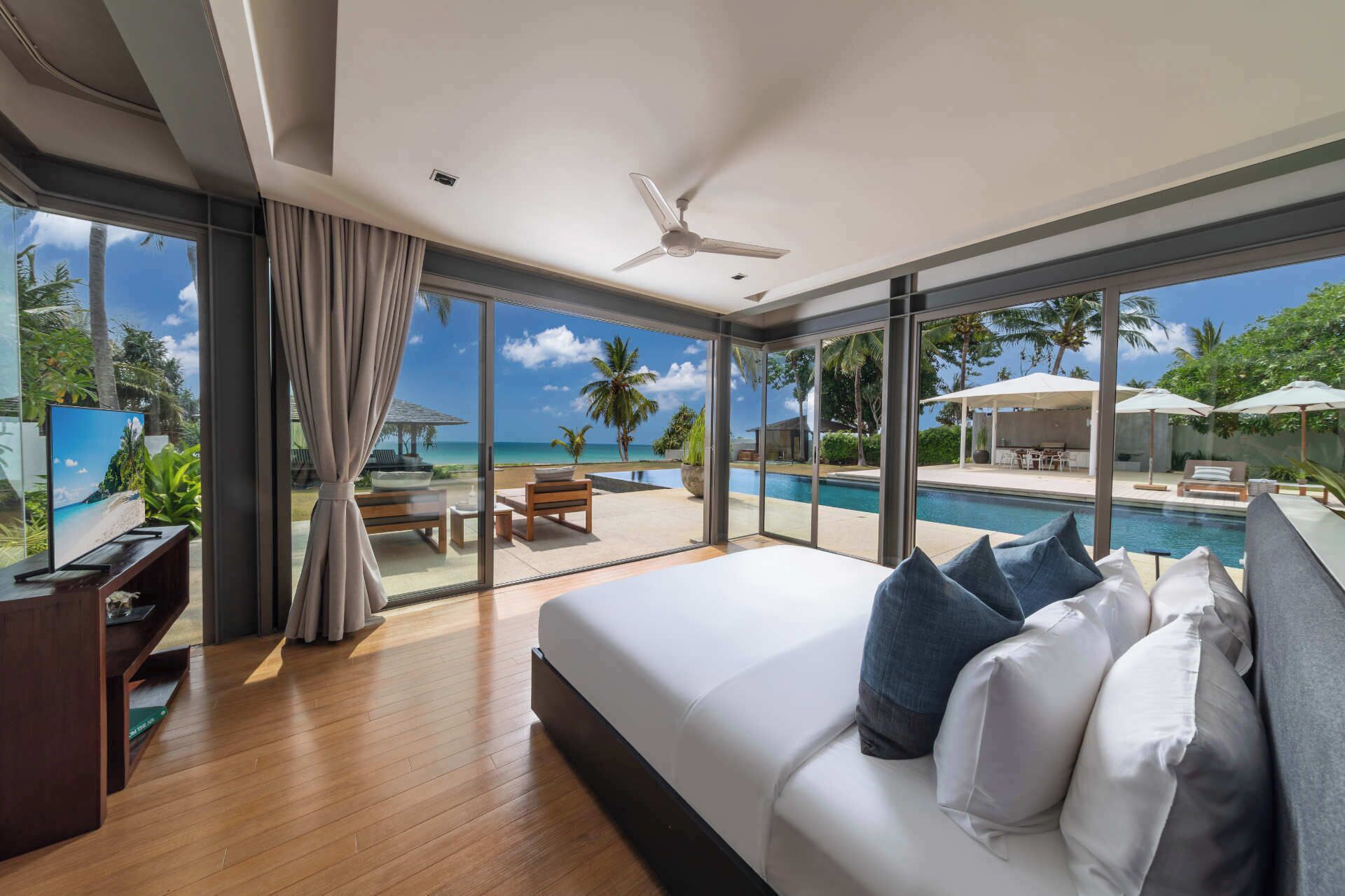 Un dormitorio moderno con una cama grande, televisión y vistas a una piscina y zona de estar exterior.