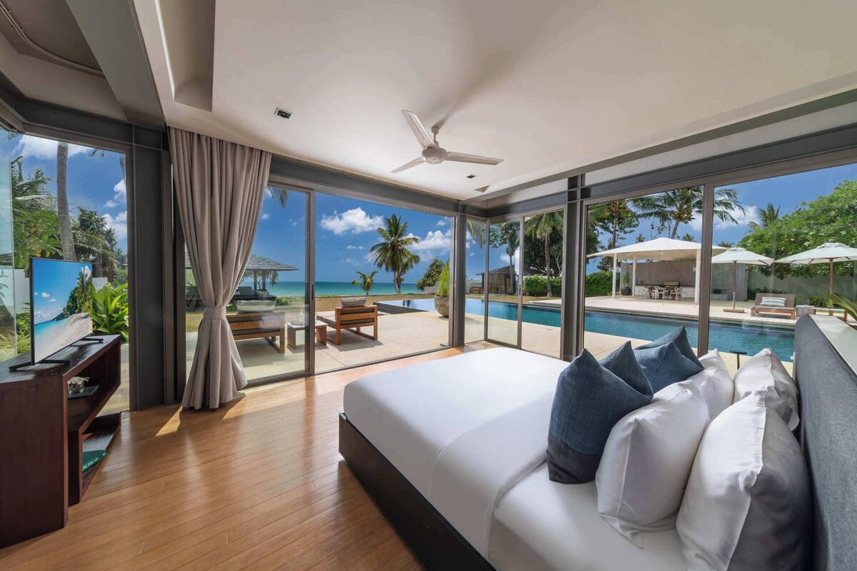 A modern bedroom with a large bed, a TV, and a view of a pool and outdoor seating area.