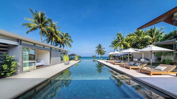 Un hôtel moderne doté d’une piscine à débordement, de chaises longues et de palmiers.
