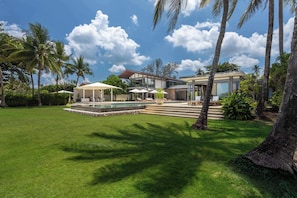 A modern house with a swimming pool, outdoor seating, and palm trees.