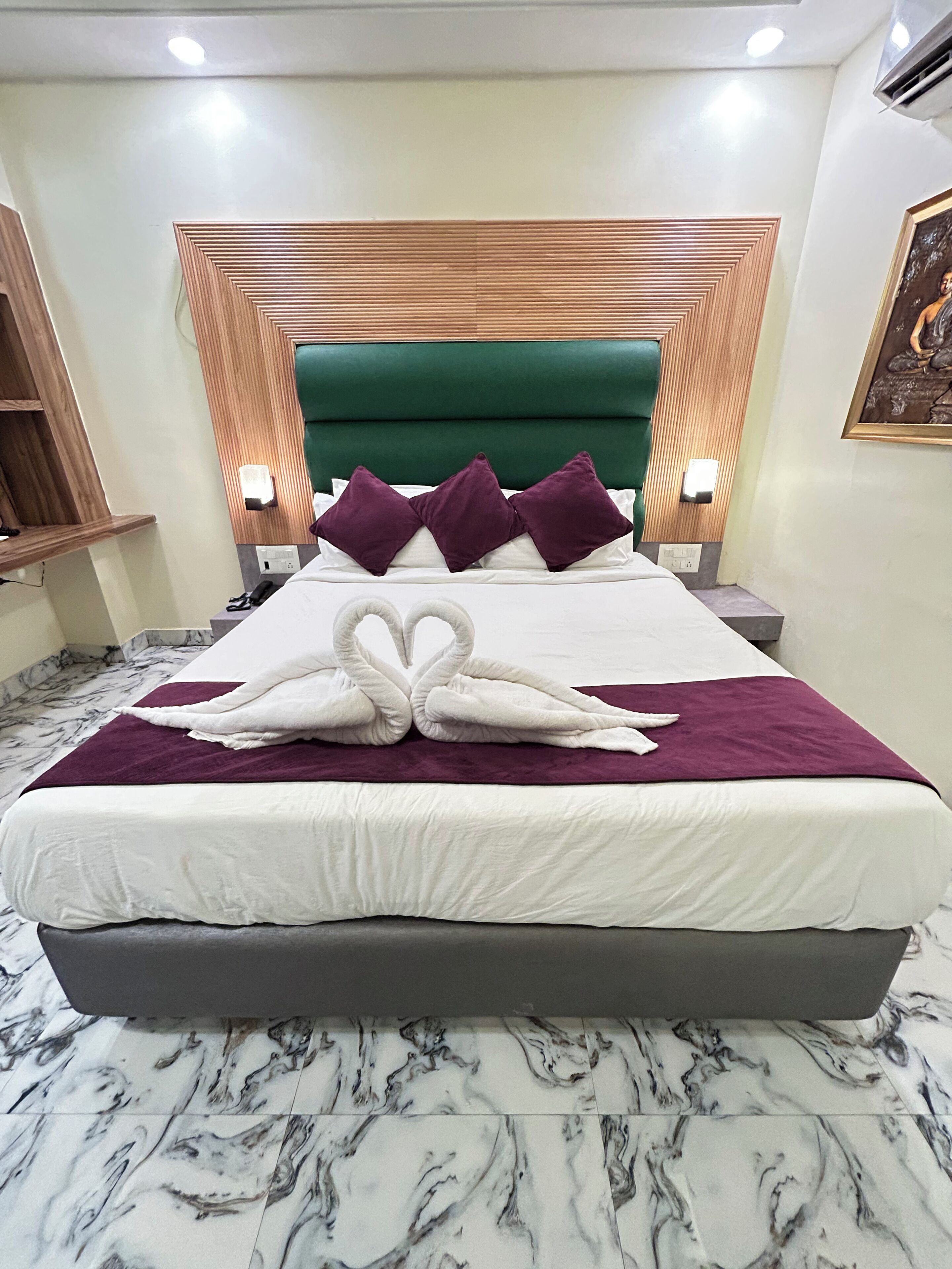 Una habitación de hotel con una cama grande, cabecera verde y suelo de mármol.