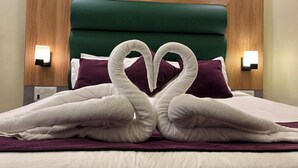 A hotel room with a bed featuring a heart-shaped towel arrangement and a wooden headboard. - All Season Residency (Port Blair)