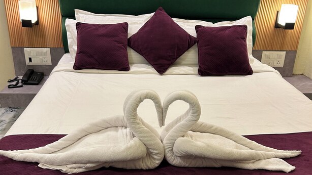 A neatly made bed with a heart-shaped towel arrangement, a green upholstered headboard, and two bedside lamps. - All Season Residency (Port Blair)