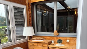Een houten interieur met een groot raam, een lamp, een dressoir en een klein tafeltje met een plant.