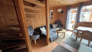Een gezellig houten interieur met een bank, stoelen, een eettafel en een trap.
