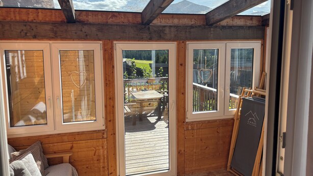 Een houten kamer met een dakraam, een schuifdeur naar een terras buiten, en een bed met kussens.