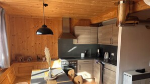 Een houten interieur met een eettafel, stoelen, een fornuis en een koelkast.