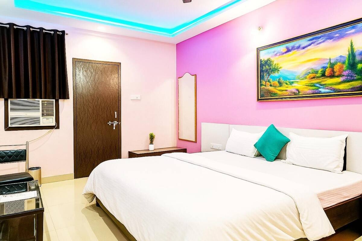 A hotel room with a bed, a bedside table, a mirror, and a painting on the wall.