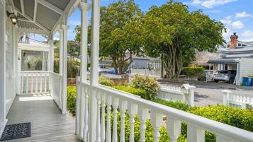A covered porch with a white railing, a view of a residential street, and a large tree in the background.