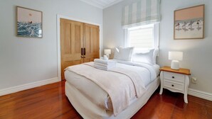 A bedroom with a large bed, wooden wardrobe, bedside tables with lamps, and artwork on the walls. - Best of Both Worlds` Gorgeous Villa near Beaches (Auckland North Shore)