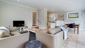A living room with a sofa, TV, and a small table. There is a staircase leading to a kitchen and dining area. - Best of Both Worlds` Gorgeous Villa near Beaches (Auckland North Shore)