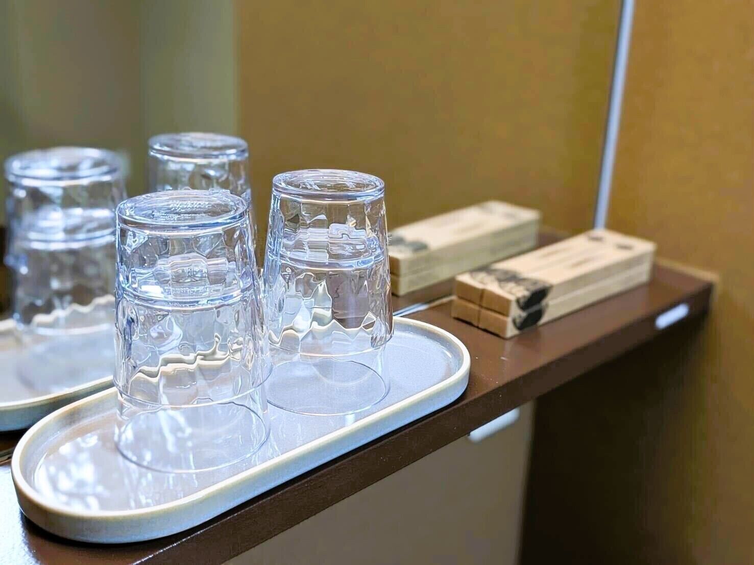 A tray with three clear glasses and a box of tissues on a wooden counter.