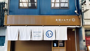 Un bâtiment à deux étages, avec un étage supérieur bleu et un étage inférieur marron. Au rez-de-chaussée, on trouve une enseigne avec des caractères japonais et un logo.