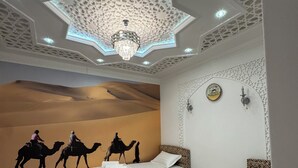 A bedroom with a large bed, a smaller bed, a nightstand, a wall-mounted clock, and a ceiling with intricate patterns and a chandelier. - Meros Guest House (Samarkand)