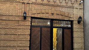 A brick building with a decorative entrance featuring a metal gate and two wall-mounted lanterns. - Meros Guest House (Samarkand)